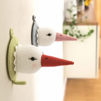 Crochet stork heads hanging on the wall and serving as coat hooks