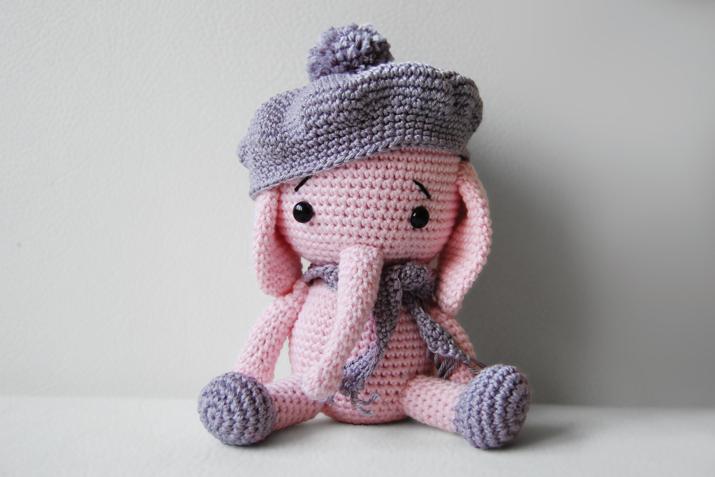 Cute crochet elephant wearing grey hat and scarf, sitting on the grey sofa.