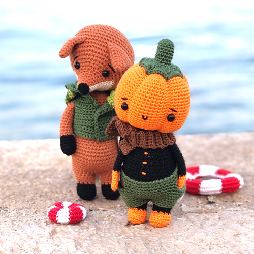 Crochet pumpkin and fox dolls standing on the beach with lifebelts scattered around.