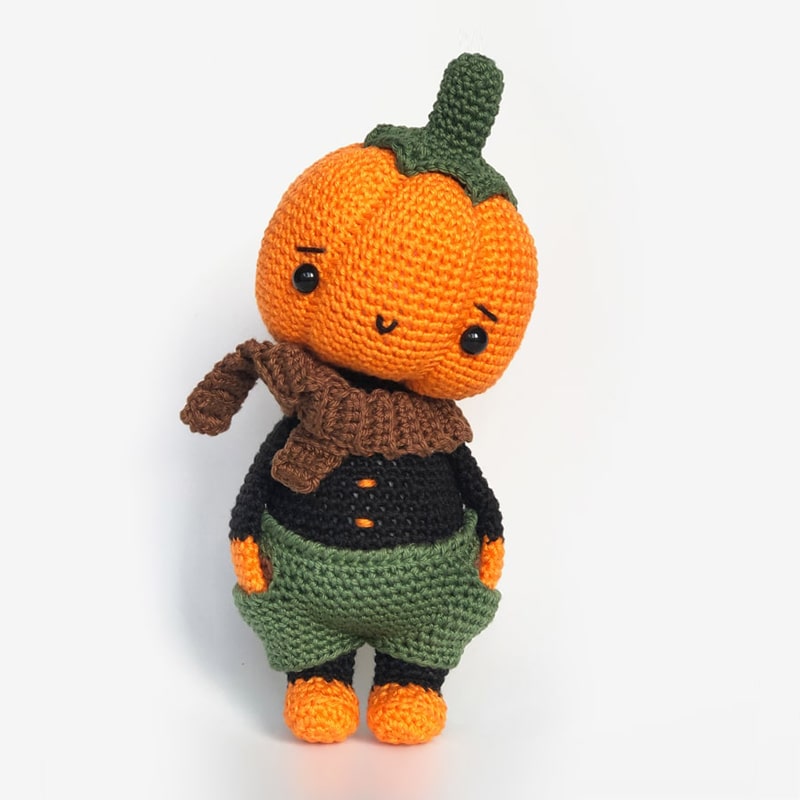 Crochet pumpkin doll wearing brown scarf and green shorts