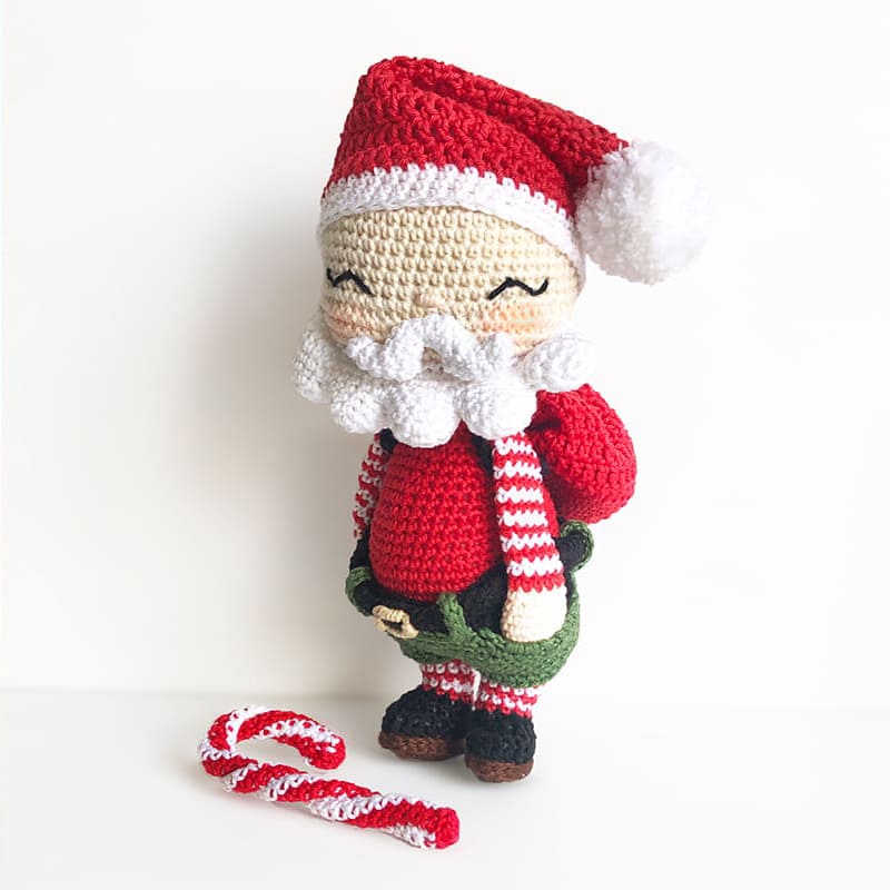 Amigurumi crochet Santa Claus with hat on the head, gift sack and candy cane as a Christmas decor.