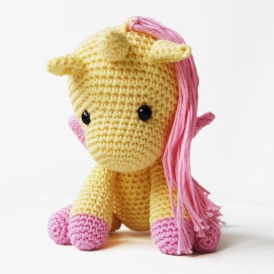 Amigurumi crochet unicorn, with pink mane and wings, crocheted in yellow cotton yarn