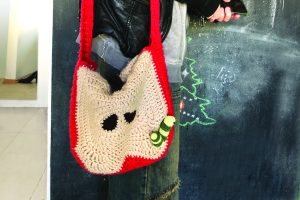 A handmade crochet apple slice bag with seeds and a leafy stem, hanging on a girl's shoulder. A playful crochet snail is attached to the bag, adding a whimsical touch. The girl demonstrates the bag’s size and shape, showcasing its stylish and functional design—ideal for adding a unique, handmade accent to any outfit.